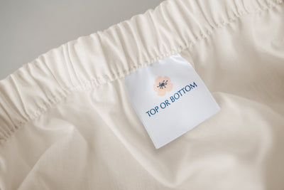 Fitted 100% USA cotton natural sheet showing tag. for where the top or bottom of the bed should be.