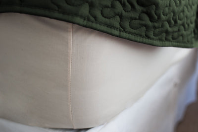 Corner of mattress made with cotton fitted sheet in natural color with a green bedspread.