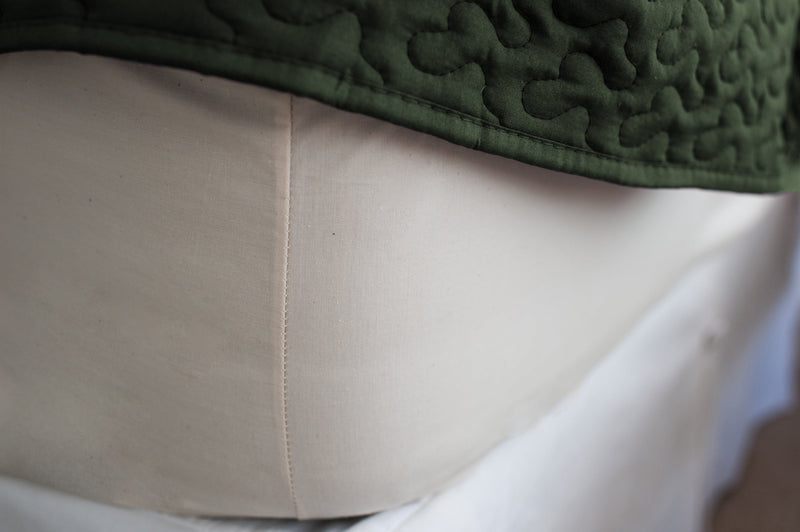 Corner of mattress made with cotton fitted sheet in natural color with a green bedspread.