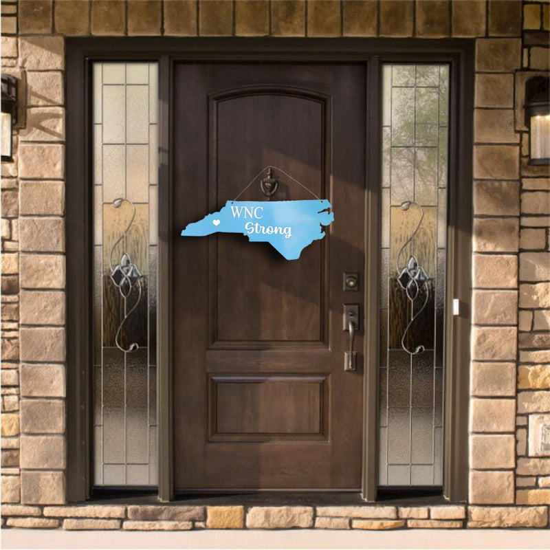 Brown door with decorative blue "Western North Caroline Strong" sign on a stone wall background.