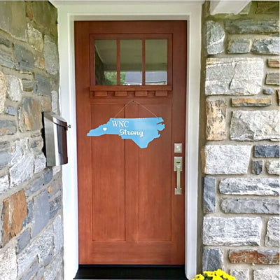 Wooden door with a blue North Carolina-shaped sign reading 'WNC Strong' against a stone wall.