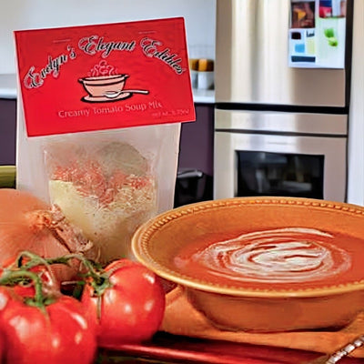 Bag of Evelyn's Elegant Edibles Creamy Tomato Soup Mix with a bowl of soup and tomatoes in a kitchen setting.