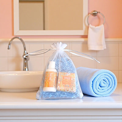 Bathroom setting with Juicy Peach Mini Soap, Lotion, and Soap Saver Gift Bag on rolled towel. Like a mini spa experience from Harvest Array.