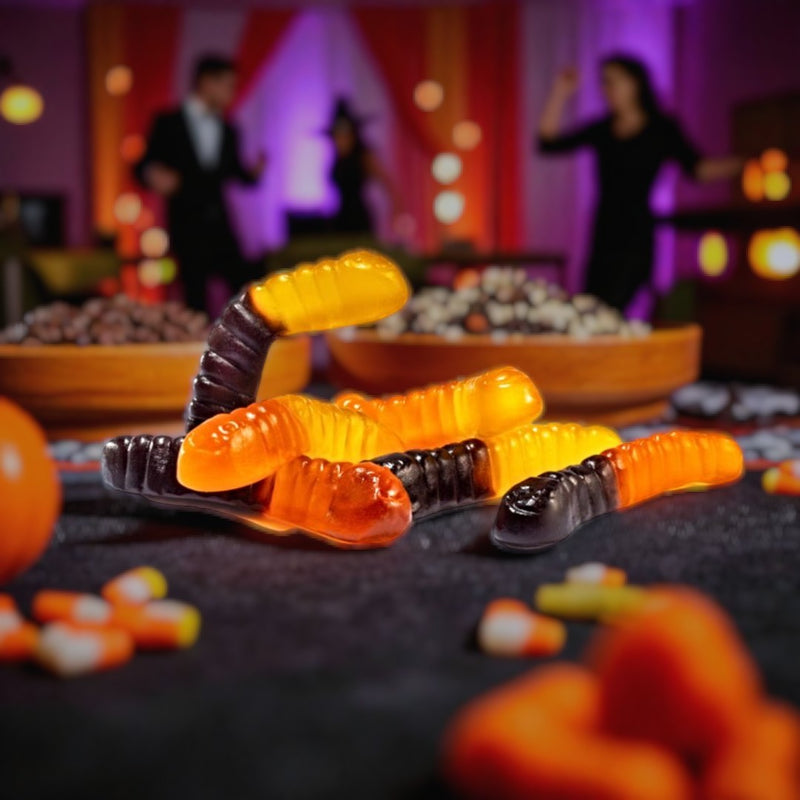 Gummy worms on a plate with Halloween-themed decorations in the background