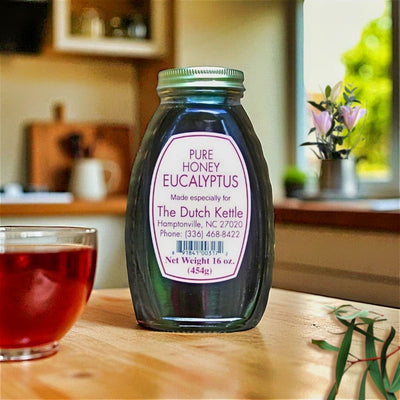 Bottle of Pure Eucalyptus Honey on a table with a glass of tea in a kitchen setting. Purchase online at Harvest Array.