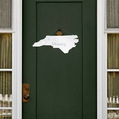 White 'WNC Strong' sign shaped like North Carolina on a green door. available now on Harvest Array.