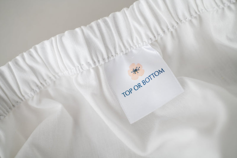 Fitted white cotton sheet showing American Blossom Linens tag for either the Top or Bottom of the bed.