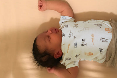 Baby in crib laying face up on organic crib sheet in natural color.