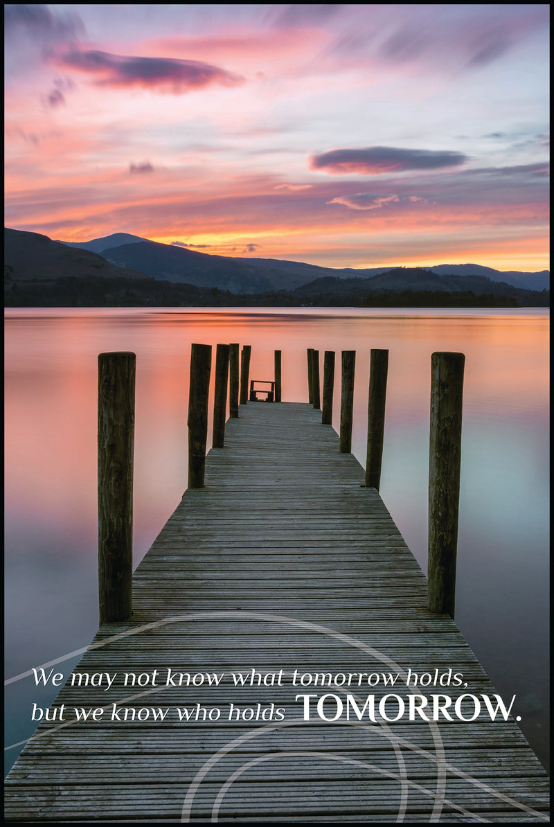 "We may not know what tomorrow holds, but we know who holds Tomorrow." with wooden dock on lake with mountains at sunset in background.