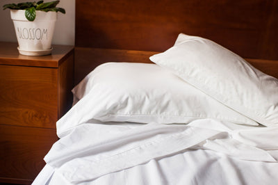 Unmade bed with cotton sheets in white color. Made in America.