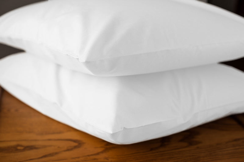 White organic cotton pillowcases with pillows stacked on a nightstand. (Pillows not included)